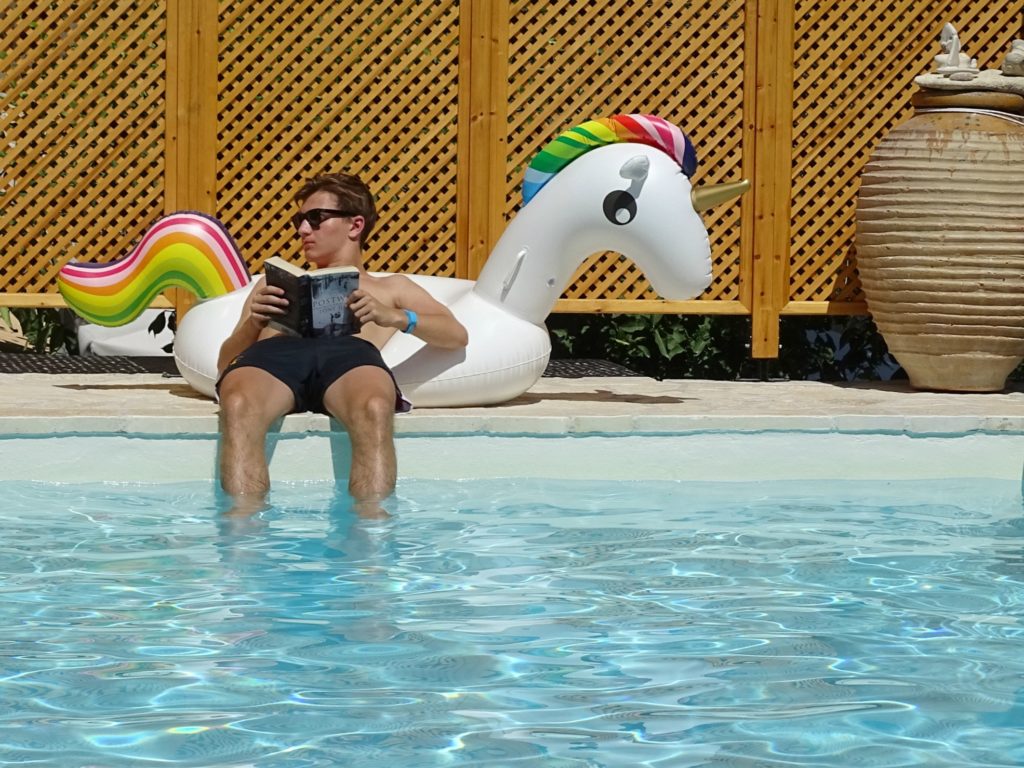 Paxos holidays, boy reading by pool with pool toy unicorn at Villa Avra Copyright©2017 mapandfamily.com 