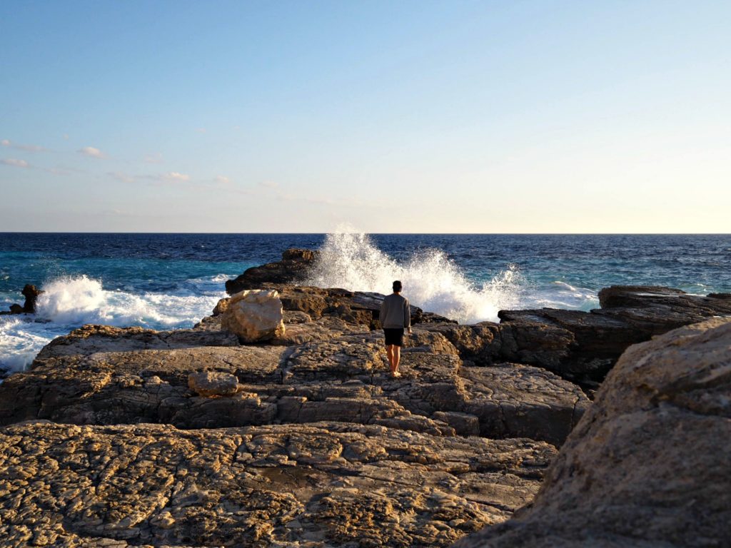 Person watches waves crashing on rocks at Plani beach, Paxos. Copyright©2017 mapandfamily.com 