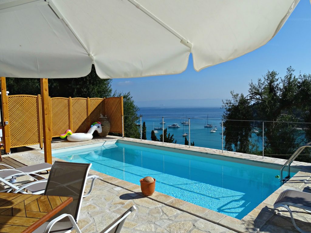 Terrace at Villa Avra with umbrella and view of bay beyond the pool. Copyright © 2017 mapandfamily.com 