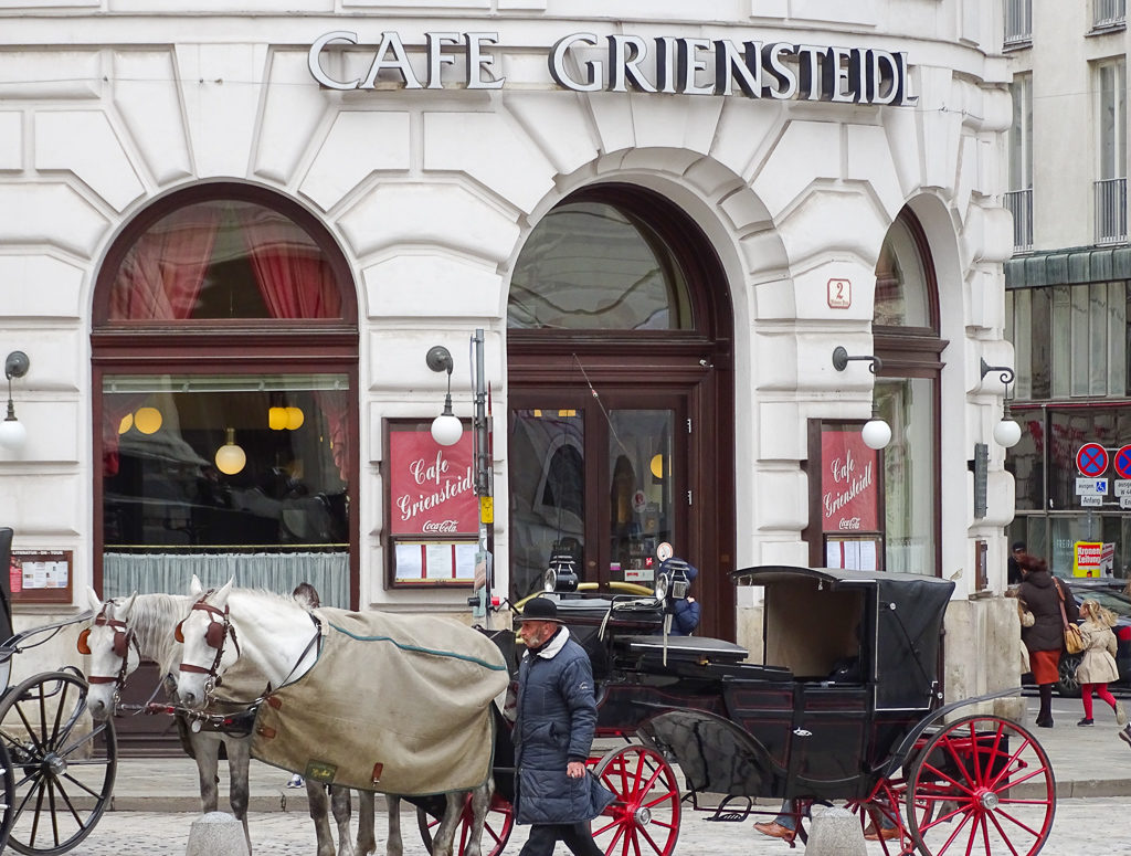 Horses and. carriage outside a grand cafe in Vienna. The horses are wearing rugs. Copyright@2024 mapandfamily.com 