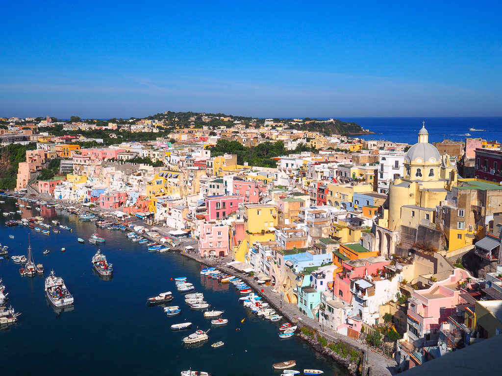 Pastel-coloured houses in a hilside surrounding a little harbour on Procida island near Naples Italy. Copyright@2024 mapandfamily.com