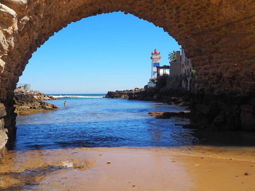 View of blue and white Santa Marta lighthouse through arch of bridge above cove. Copyright ©2019 mapandfamily.com 