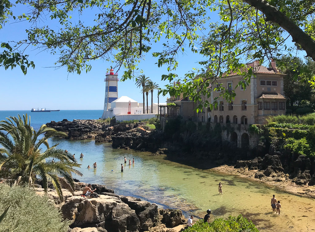 Things to do in Cascais, Portugal. Blue and white striped lighthouse in cove. Copyright ©2019 mapandfamily.com 