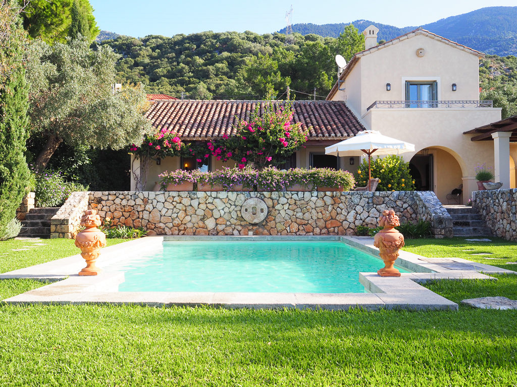 Villa with tiled roof and pink flowers growing on terrace overlooking pool with terracotta pots. Copyright ©2019 mapandfamily.com 