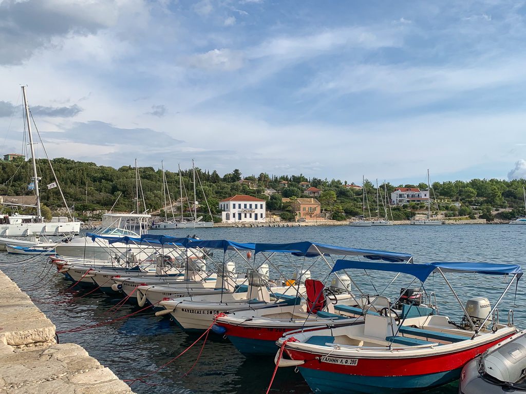 Fiscardo villas. Boats moored at quay and villas on the hillside in the background. Copyright ©2020 mapandfamily.com 