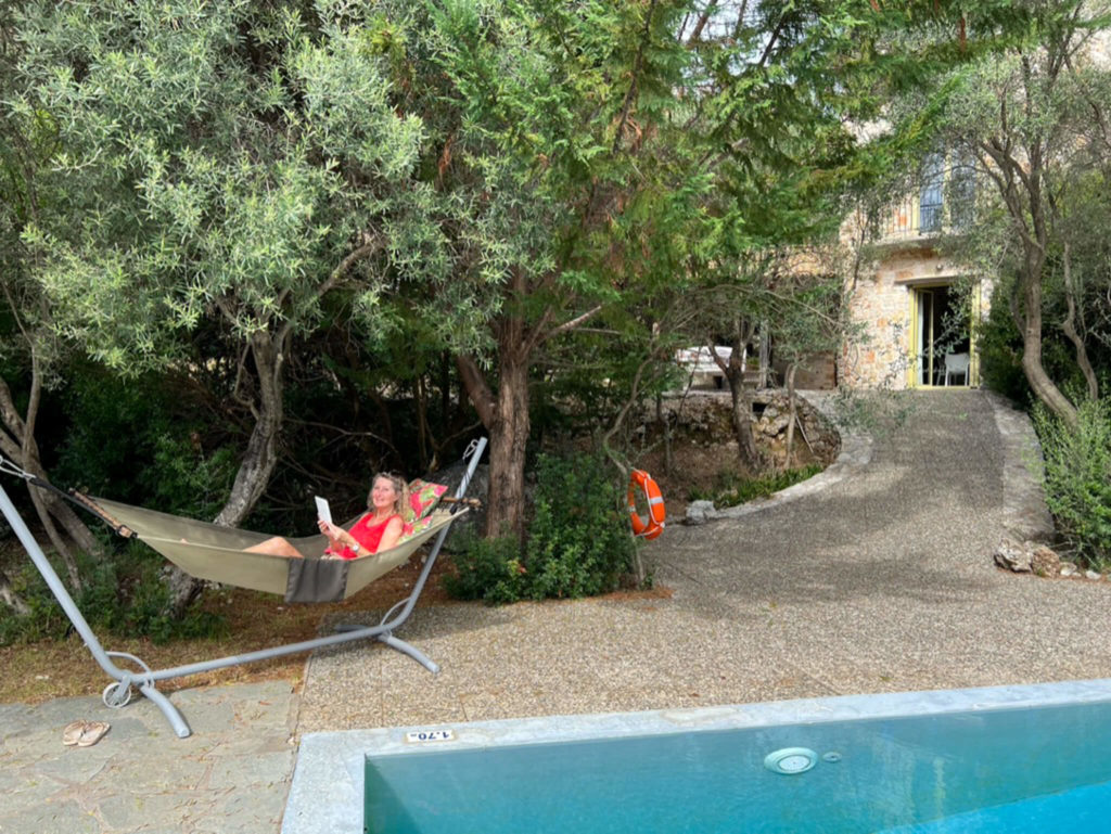 Woman in red top reading a book in a hammock in garden of Villa Thimari, Vasiliki. Copyright@ 2022 mapandfamily.com 