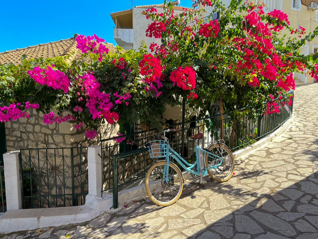 A cobbled street in Spartochori, Meganisi with pink flowers and blue bicycle. Copyright@ 2022 mapandfamily.com