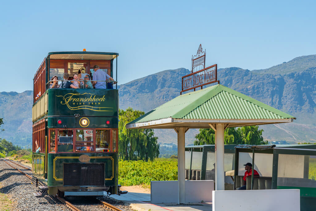 The green vintage style Franschoek wine tram pulling up to a stop. @ggfoto via DepositPhotos