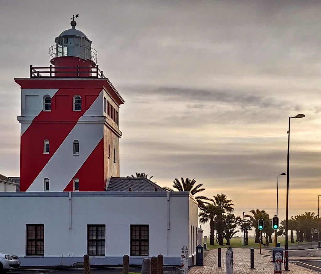 Red and white striped lighthouse in urban coastal setting with traffic lights and palm trees. Copyright@2023 reserved to photographer via mapandfamily.com 