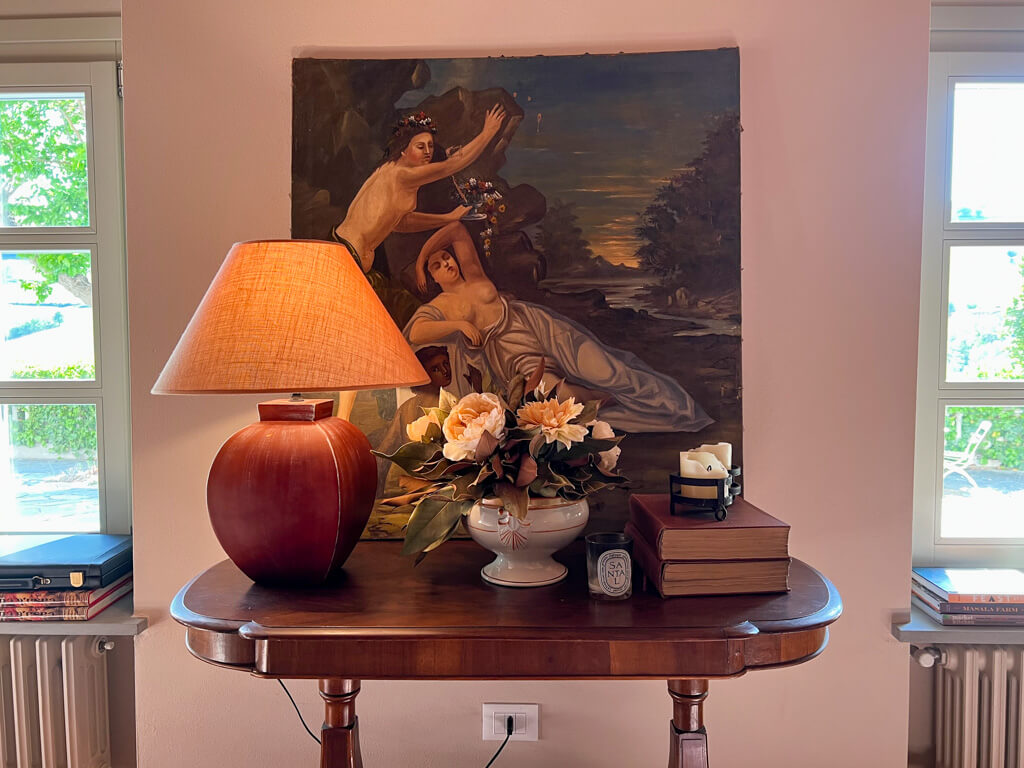 Detail of side table with lamp, books, candles and a painting behind it. Copyright@2023mapandfamily.com