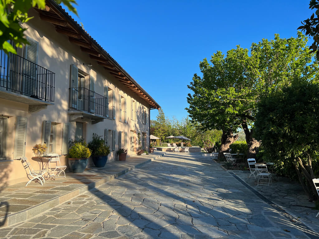 Terrace outside Villa Giara, showing white metal chairs and tables and pool parasols in background. Copyright@2023mapandfamily.com