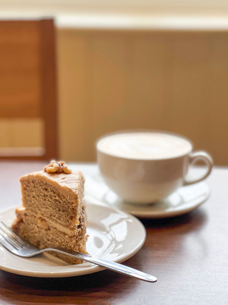 Gallery of photos of cafe on Wimbledon common. Exterior shot with windmill in background, photo of coffee and walnut cake and image of interior with tables and chairs and mural of Common on wall. Copyright@2023 mapandfamily.com 