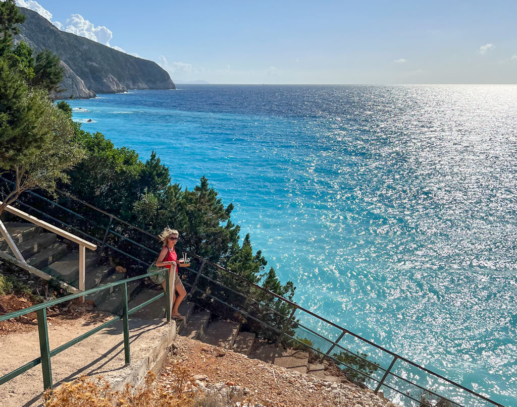 Woman walking down steep stairway to turquoise water at Porto Katsiki beach Lefkada. Copyright@2023mapandfamily.com 