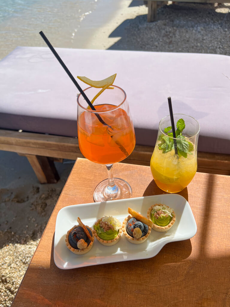 Orange and yellow coloured cocktails and canapes on table on beach Lefkada. Copyright@2023mapandfamily.com 