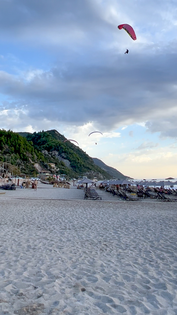 Paragliders descend from dark clouds over Kathisma beach Lefkas. Copyright@2023mapandfamily.com 