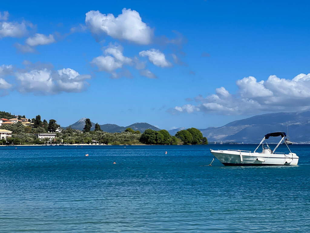 A still calm blue bay with a small white boat moored in foreground. Copyright@2023mapandfamily.com 