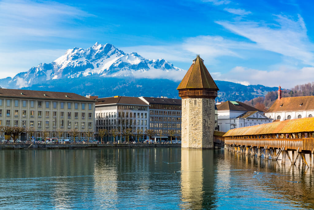  A view of the covered wooden bridge in Lucerne with snow topped mountains in background. Copyright@2023depositphotos