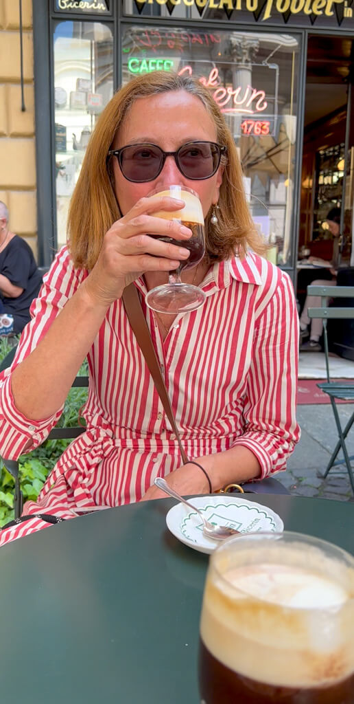 Woman in red striped dress sipping bicherin cream topped coffee from glass outside cafe in Turin. Copyright@2023 mapandfamily.com