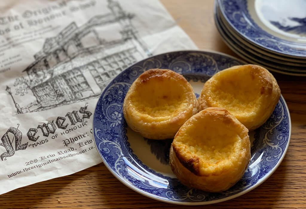 Historic London snacks; three maid of honour tarts on a blue and white plate with a bag from Newens shop. Copyright@2023 mapandfamily.com 