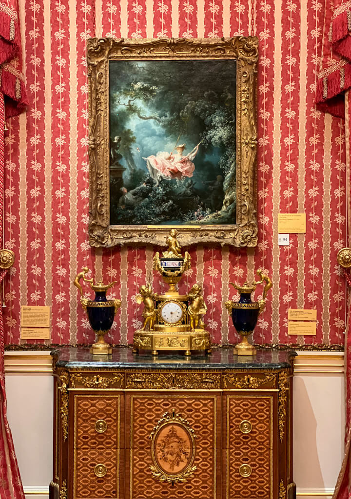 Painting of girl on swing in elaborate gilded frame against red and gold wallpaper. Copyright@2023 mapandfamily.com