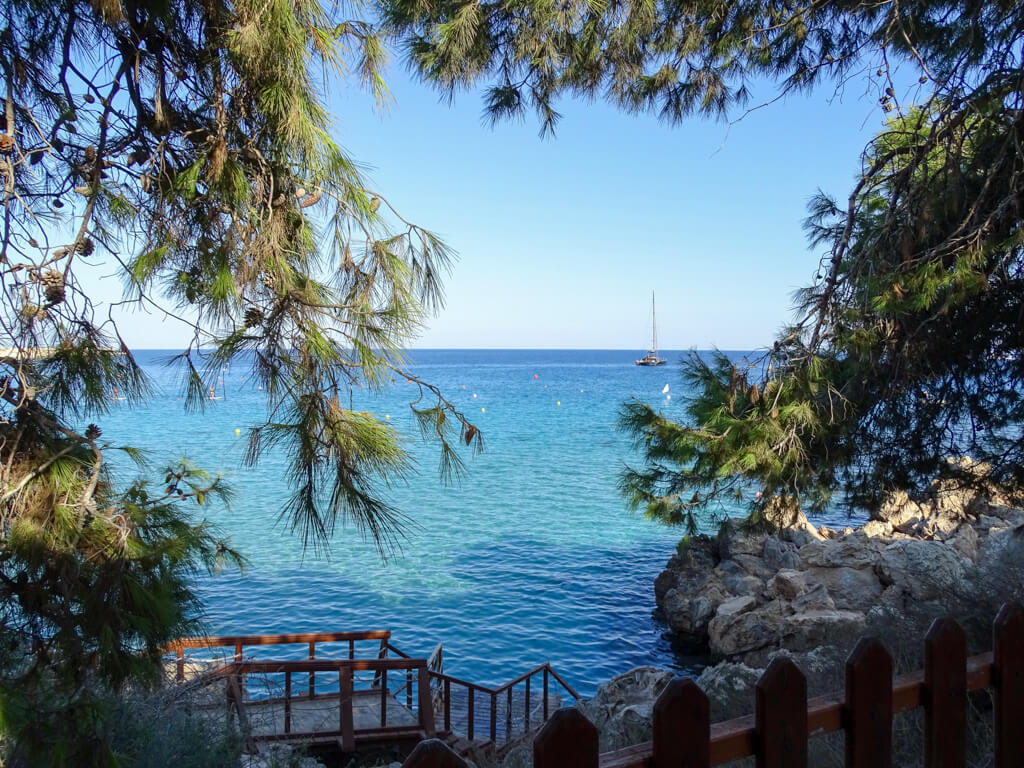 Where is hot in April in Europe? View of a cove in Cyprus with branches framing a blue sea view. Copyright@2024 Nancy Roberts mapandfamily.com 