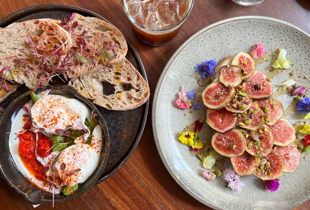 Two brunch plates, one with figs and flowers, the other with eggs in a dish and sourdough Copyright@2024mapandfamily.com 