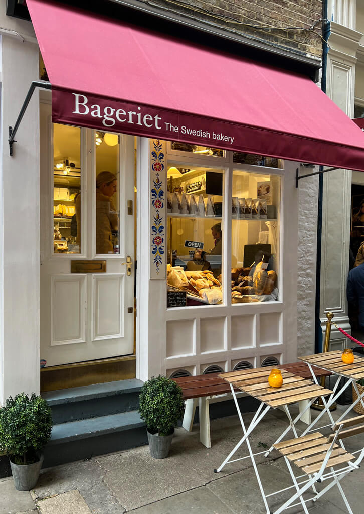 Exterior of cafe with dark red awning and slatted tables and chairs outside. Copyright@2024mapandfamily.com 