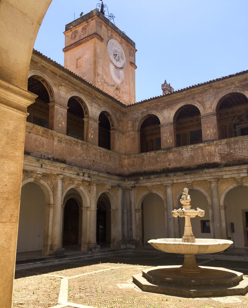 Beautiful warm stone arches and porticos in a courtyard with fountain at Certosa di Padula. Copyright@2024 reserved to the photographer via mapandfamily.com 