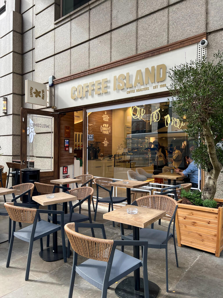 Exterior of coffee shop in Covent Garden with modern tables and chairs outside and an olive tree in pot. Copyright@2024mapandfamily.com 