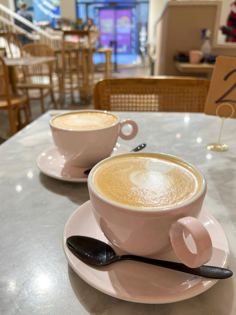 Coffee in two pink cups and saucers with black spoons on a table in cafe. Copyright@2024mapandfamily.com 