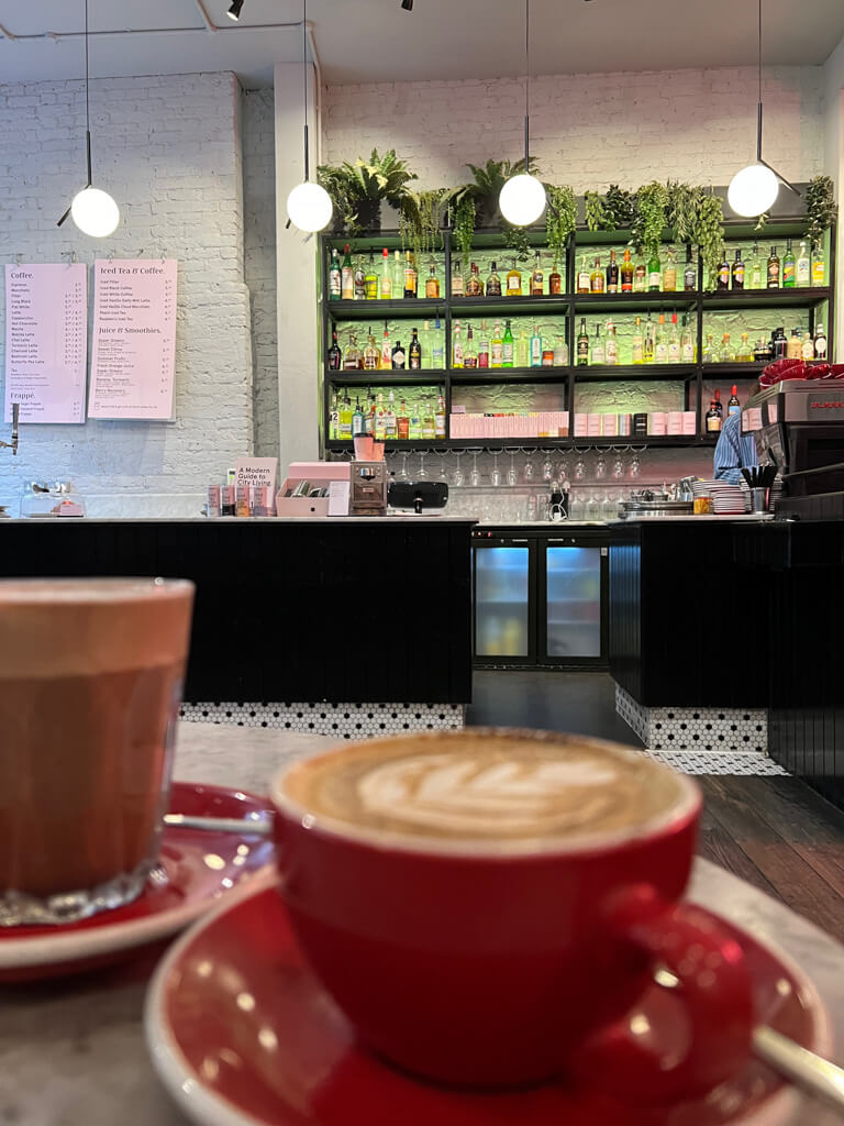 Red cup and saucer in foreground with Covent Garden coffee shop counter in background and bottles on display on wall shelving. Copyright@2024mapandfamily.com 