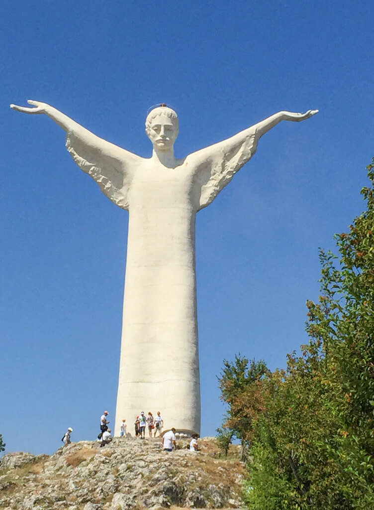 The striking figure of Cristo di Maratea, white against a deep blue sky and dwarfing the small group of people at its base. Copyright@2024 reserved to the photographer via mapandfamily.com 