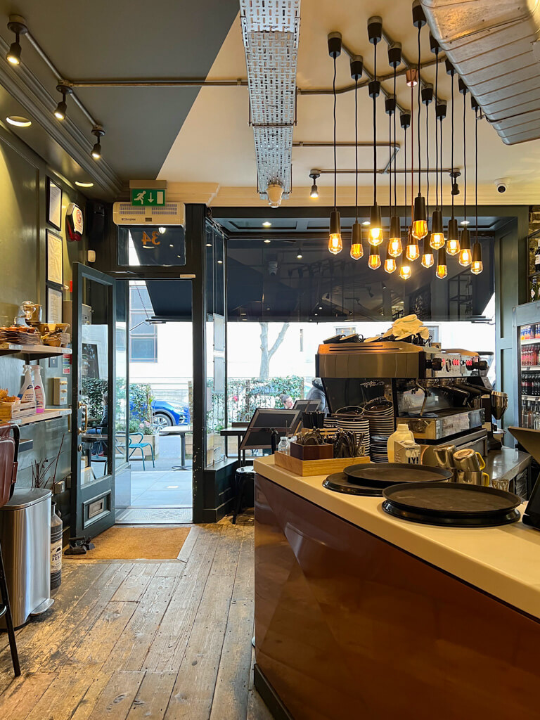 Interior of Covent Garden coffee shop the Black Penny with wooden floors and modern lighting feature over counter. Copyright@2024mapandfamily.com 