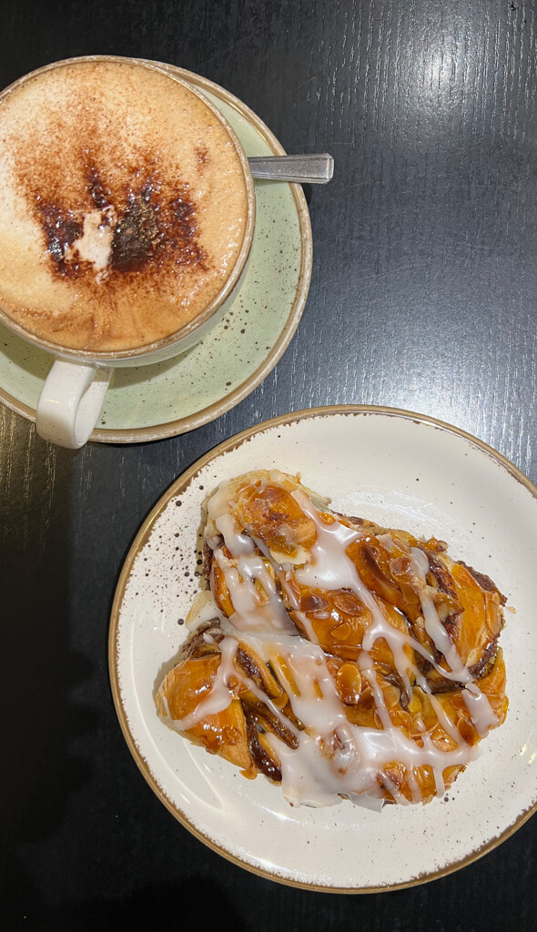 Overhead view of a cup and saucer with a cappuccino  and an iced pastry  on a plate. Copyright@2024 mapandfamily.com