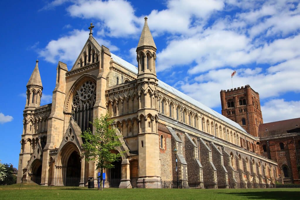 The golden toned and turreted cathedral of St Albans against a blue sky.