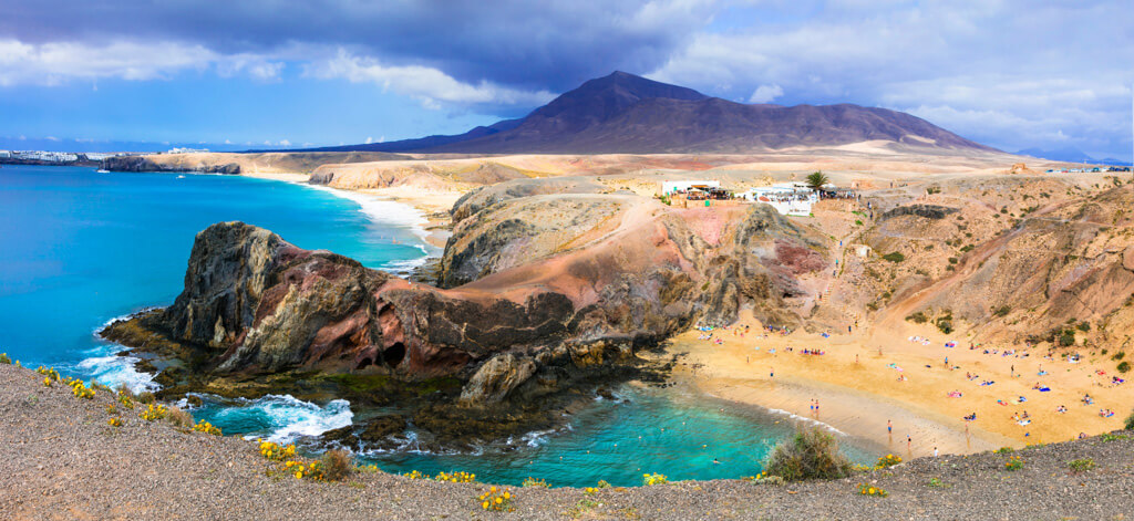 View of the Lanzarote coastline and a remote sandy beach with scattered people on it.