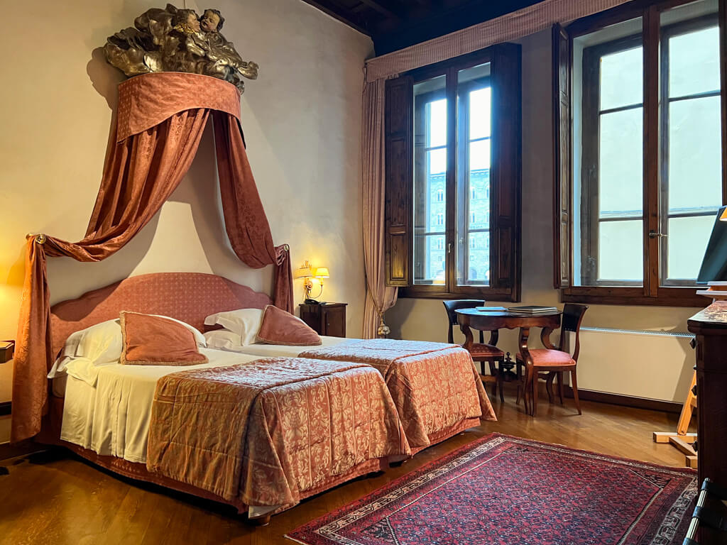 An elegant double bed with coronet and drapes in a bedroom decorated in Tuscan style in Hotel In Piazza della Signoria. Copyright@2024 NancyRoberts 