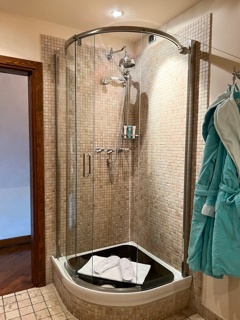 A marble-tiled corner shower in the hotel with turquoise dressing gowns hanging beside it. Copyright@2024 NancyRoberts 